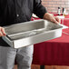 A person holding an American Metalcraft stainless steel water pan for a rectangular chafer.