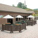 A brown Grosfillex resin patio fence around tables and chairs on an outdoor patio.