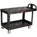 A black Rubbermaid large flat two shelf utility cart with wheels.