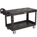 A black Rubbermaid plastic utility cart with two flat shelves and wheels.