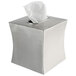 A brushed stainless steel square tissue box cover with tissue sticking out.
