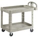 A beige Rubbermaid plastic utility cart with two shelves and a handle.
