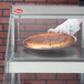 A hand in a glove holding a pizza in a Hatco heated glass display case.