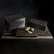 A rectangular black faux wood riser on a table with lime wedges on it.