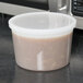 A 2 Qt. translucent plastic deli container with a lid containing brown liquid sitting on top of a microwave.