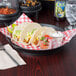 A round deli server holding tacos and salsa on a table with glasses of water.