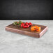 A rectangular faux walnut melamine display riser with a variety of peppers on it.