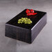 A rectangular black wooden block with a faux zebra wood pattern holding red pepper and green beans on a table in a deli.