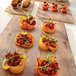 An Elite Global Solutions square faux driftwood melamine serving board with yellow bell peppers filled with tomatoes and herbs.