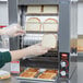 A woman in gloves putting slices of bread into a Hatco vertical conveyor toaster.