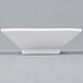 A CAC Citysquare white square porcelain bowl on a gray surface.