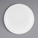 A white Elite Global Solutions round melamine plate with a rim on a gray surface.