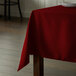 A table with a square burgundy tablecloth on it.