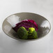 An Elite Global Solutions Pebble Creek mushroom-colored bowl filled with broccoli and cabbage on a table.