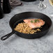 An Elite Global Solutions black faux cast iron fry pan with salmon and rice in it on a table.