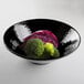 A black Elite Global Solutions melamine bowl filled with broccoli and cabbage on a white surface.