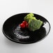 A black Elite Global Solutions round plate with broccoli and tomatoes on it.