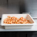 A white Cambro food pan filled with shrimp on a counter.