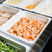 A white Cambro polycarbonate food pan with food on a buffet counter.