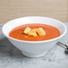 A white Elite Global Solutions melamine bowl of tomato soup with croutons.