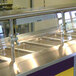 An Advance Tabco cafeteria food shield with a stainless steel counter top on a food counter.