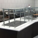 An Advance Tabco self service food shield with glass panels on a stainless steel counter.