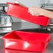 A person holding a Vollrath red plastic tray.