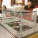 An Advance Tabco cafeteria food shield with a glass top over a stainless steel counter.