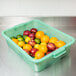 A Vollrath green Traex bus tub filled with oranges and apples on a counter.