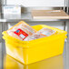 A yellow Vollrath Color-Mate drain box filled with food on a counter.