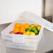 A Vollrath Color-Mate clear plastic food storage container with limes and oranges inside.