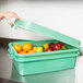 A woman using a Vollrath green plastic container with a lid to store oranges and red apples.