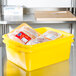 A Vollrath yellow Traex Color-Mate container filled with food on a counter.