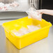 A hand putting a bag of chicken in a yellow Vollrath food storage container.