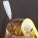 A glass of iced tea with a lemon wedge and Oneida Cityscape stainless steel spoon.