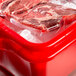 A red Vollrath Traex food storage container with raw meat wrapped in plastic inside.