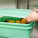 A hand opening a Vollrath Traex food storage box lid to reveal fruit inside.