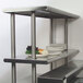 An Advance Tabco stainless steel double deck overshelf on a counter with plates and food on it.