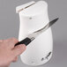 A person holding a knife in front of a white Proctor Silex electric can opener.