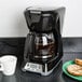 A Proctor Silex coffee maker brewing a pot of coffee on a black surface.