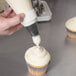 A hand using an Ateco pastry bag to frost a cupcake.