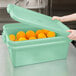 A person holding a green plastic Vollrath food storage container with oranges inside.