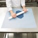 A chef using an Ateco non-stick silicone baking work mat to roll out dough on a table.