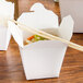 A white Fold-Pak Chinese take-out container filled with food with chopsticks on top.