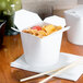 A white SmartServ take-out container with food and chopsticks on a table.