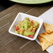 A white square Carlisle ramekin filled with guacamole and chips.
