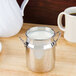 An American Metalcraft stainless steel milk can creamer on a counter next to a cup of milk.