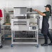 A woman and a man using a Lincoln Impinger II conveyor oven to cook a pizza.