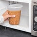 A hand holding a Pactiv translucent deli container of beans being poured into a microwave.