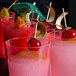 A row of red Fineline Savvi Serve plastic tumblers filled with pink drinks and cherries with straws.
